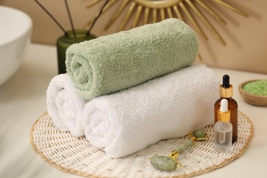 Photo of Spa composition. Rolled towels, cosmetic products and face roller on table