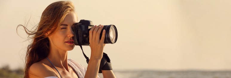 Image of Photographer taking photo with professional camera near sea, space for text. Banner design