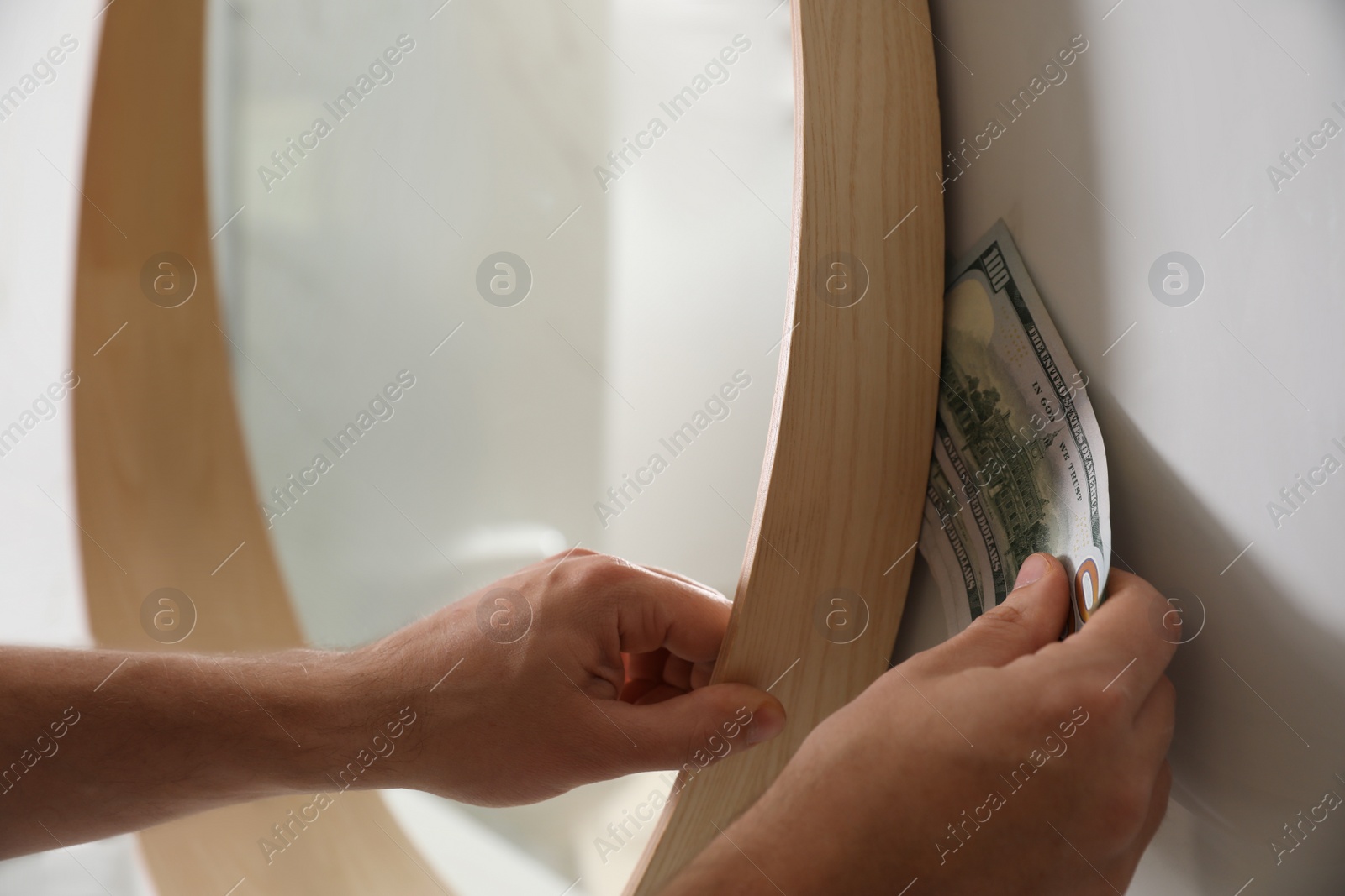 Photo of Man hiding money behind mirror indoors, closeup. Financial savings