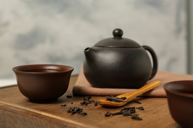 Cup of aromatic tea, dry leaves and teapot on wooden board, closeup