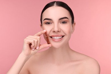 Photo of Beautiful young woman holding skincare ampoule on pink background