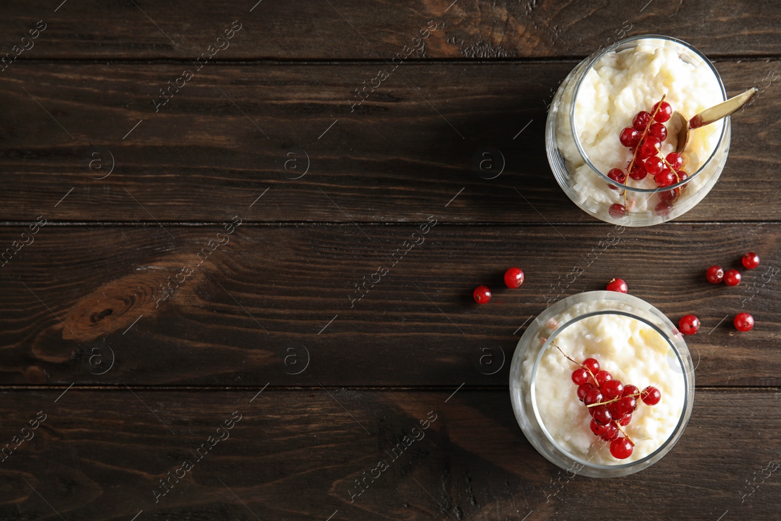 Photo of Creamy rice pudding with red currant in glasses and berries on wooden background, top view. Space for text