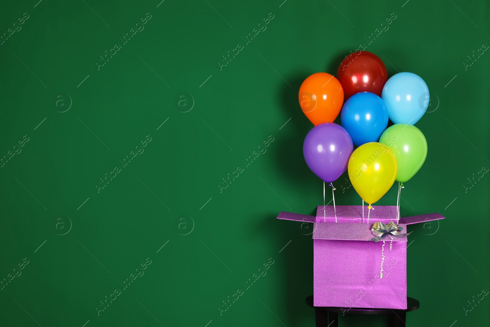 Photo of Gift box with bright air balloons on green background. Space for text