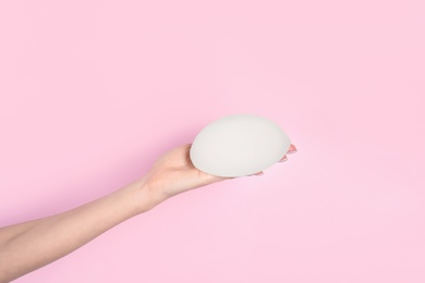 Woman holding silicone implant for breast augmentation on color background, space for text. Cosmetic surgery