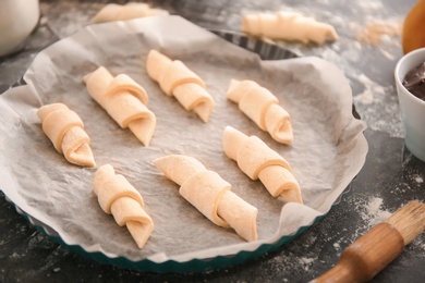 Photo of Baking dish with raw croissants on kitchen table