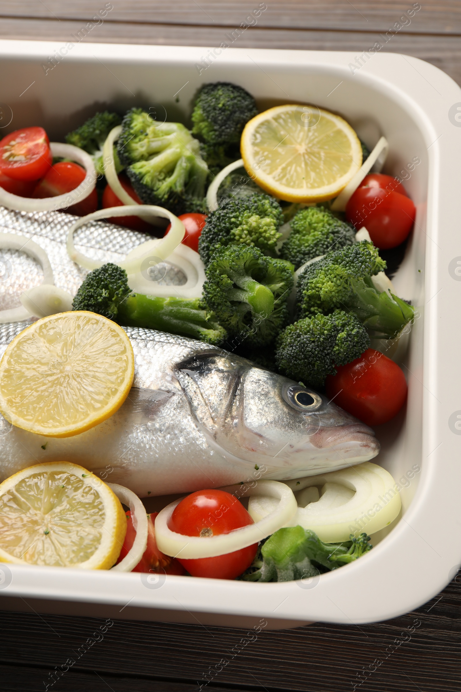 Photo of Raw fish with vegetables and lemon in baking dish on table, above view