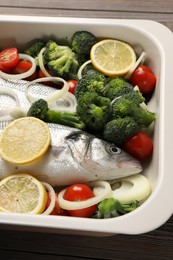 Raw fish with vegetables and lemon in baking dish on table, above view