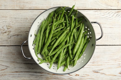 Photo of Fresh green beans in colander on white wooden table, top view