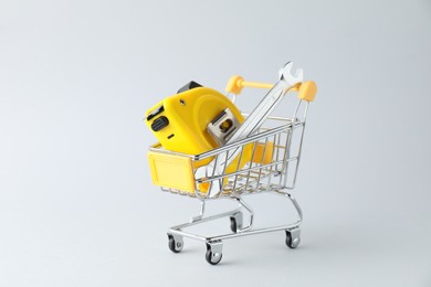 Photo of Metal wrench and measuring tape in shopping cart on light grey background
