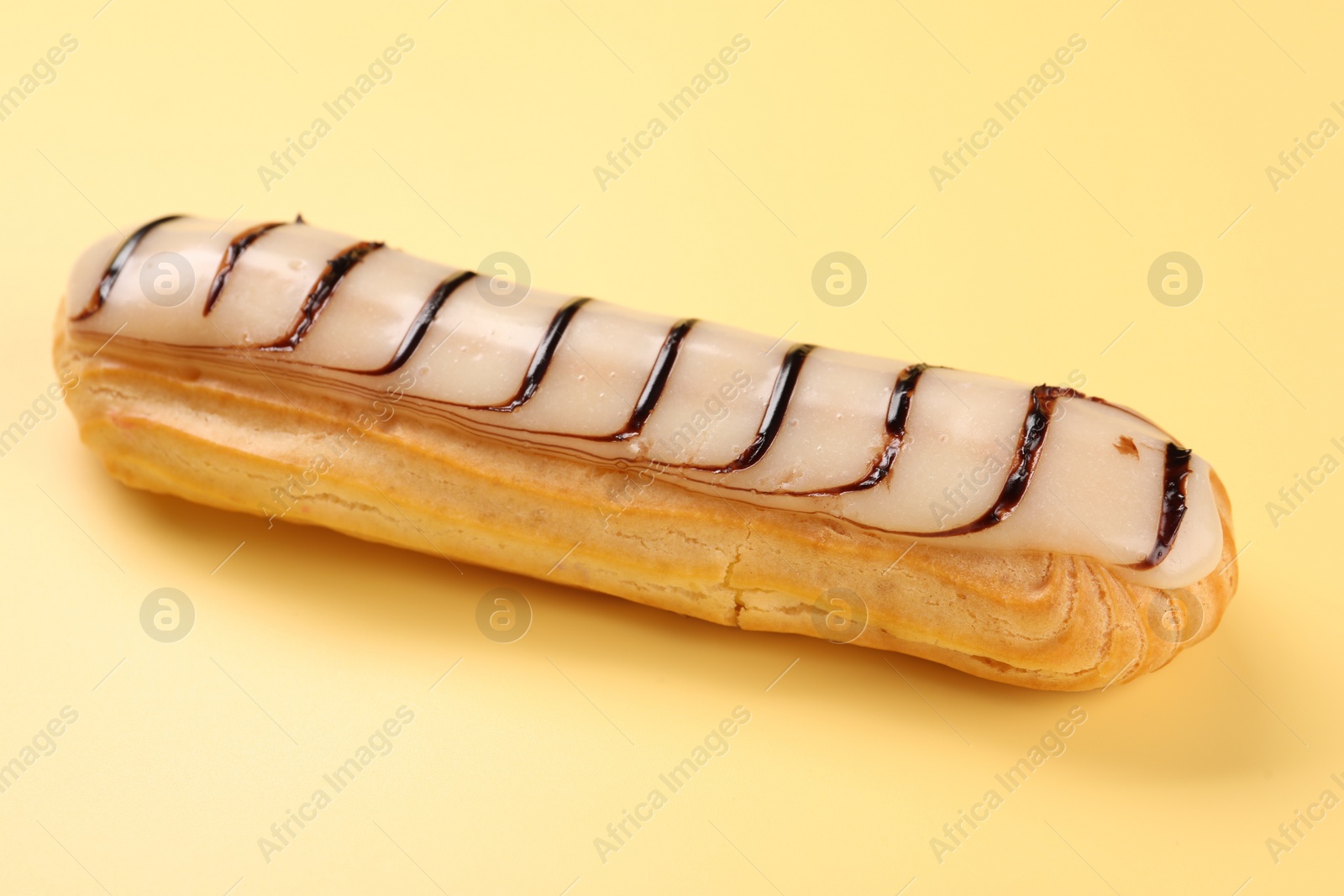 Photo of Delicious eclair covered with glaze on yellow background