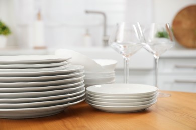 Clean plates, bowls and glasses on wooden table in kitchen