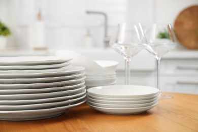 Photo of Clean plates, bowls and glasses on wooden table in kitchen