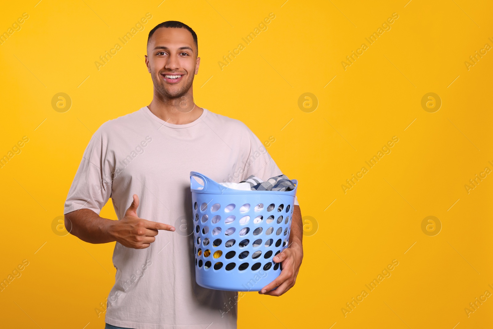 Photo of Happy man with basket full of laundry on orange background. Space for text