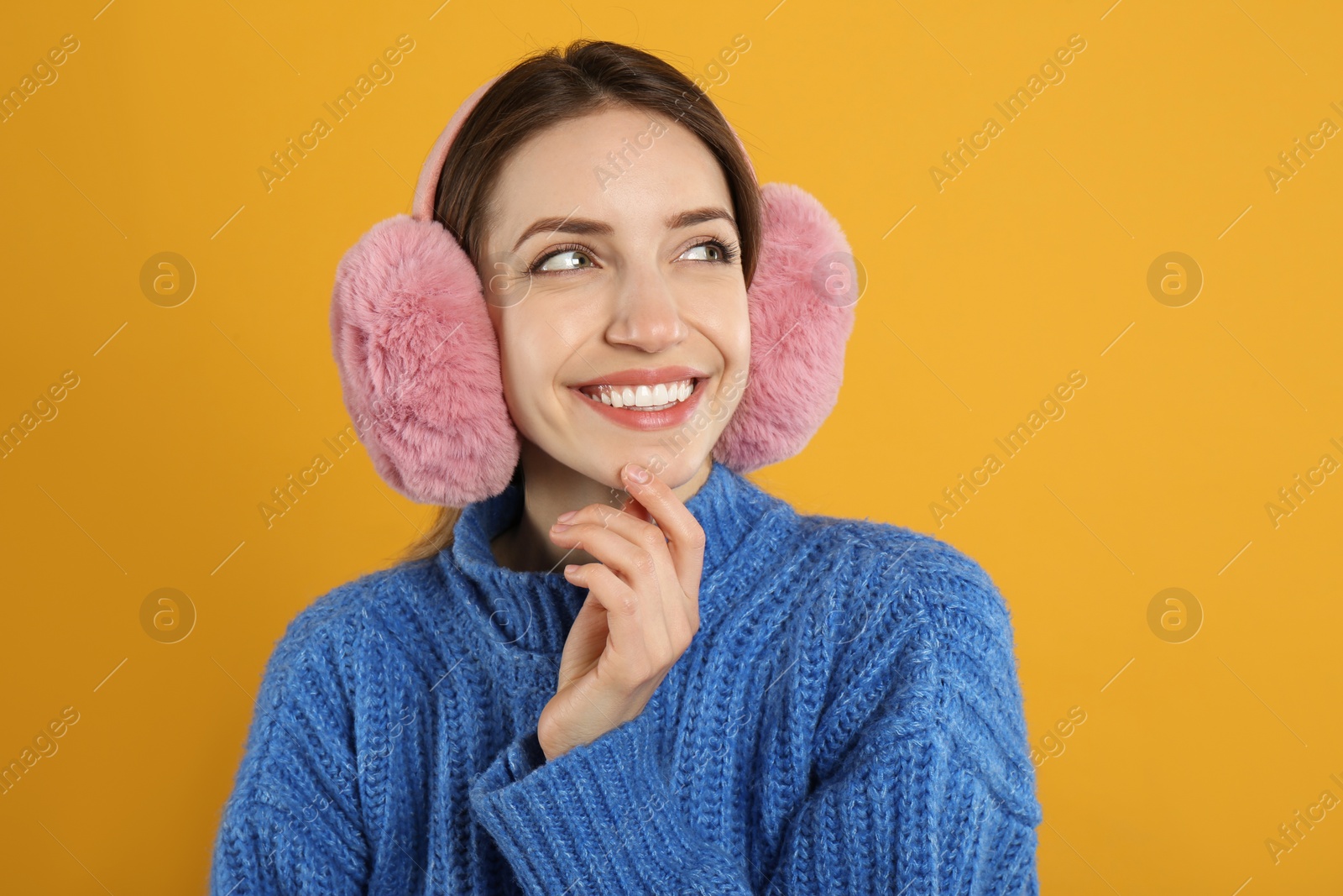 Photo of Happy woman wearing warm earmuffs on yellow background