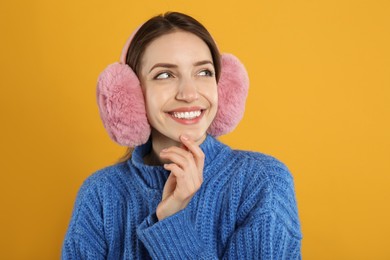 Photo of Happy woman wearing warm earmuffs on yellow background