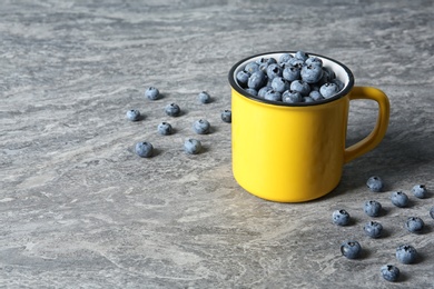 Photo of Fresh blueberries in yellow cup and space for text on color table