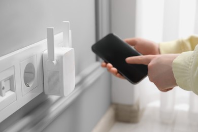 Woman using smartphone for wireless Wi-Fi repeater indoors, closeup