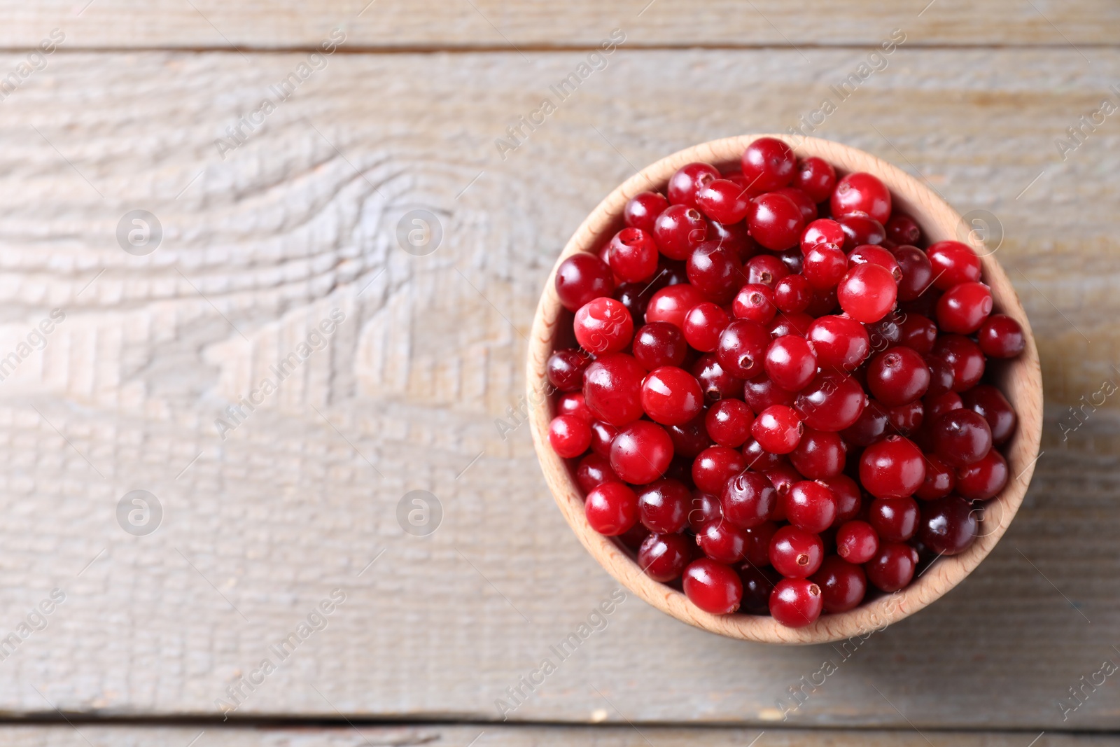 Photo of Fresh ripe cranberries in bowl on wooden table, top view. Space for text