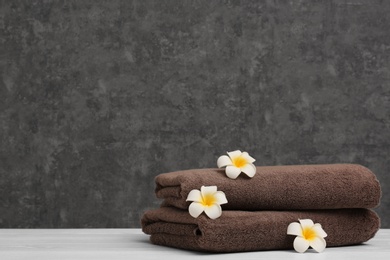 Photo of Stack of soft clean towels with beautiful flowers on table against color background. Space for text