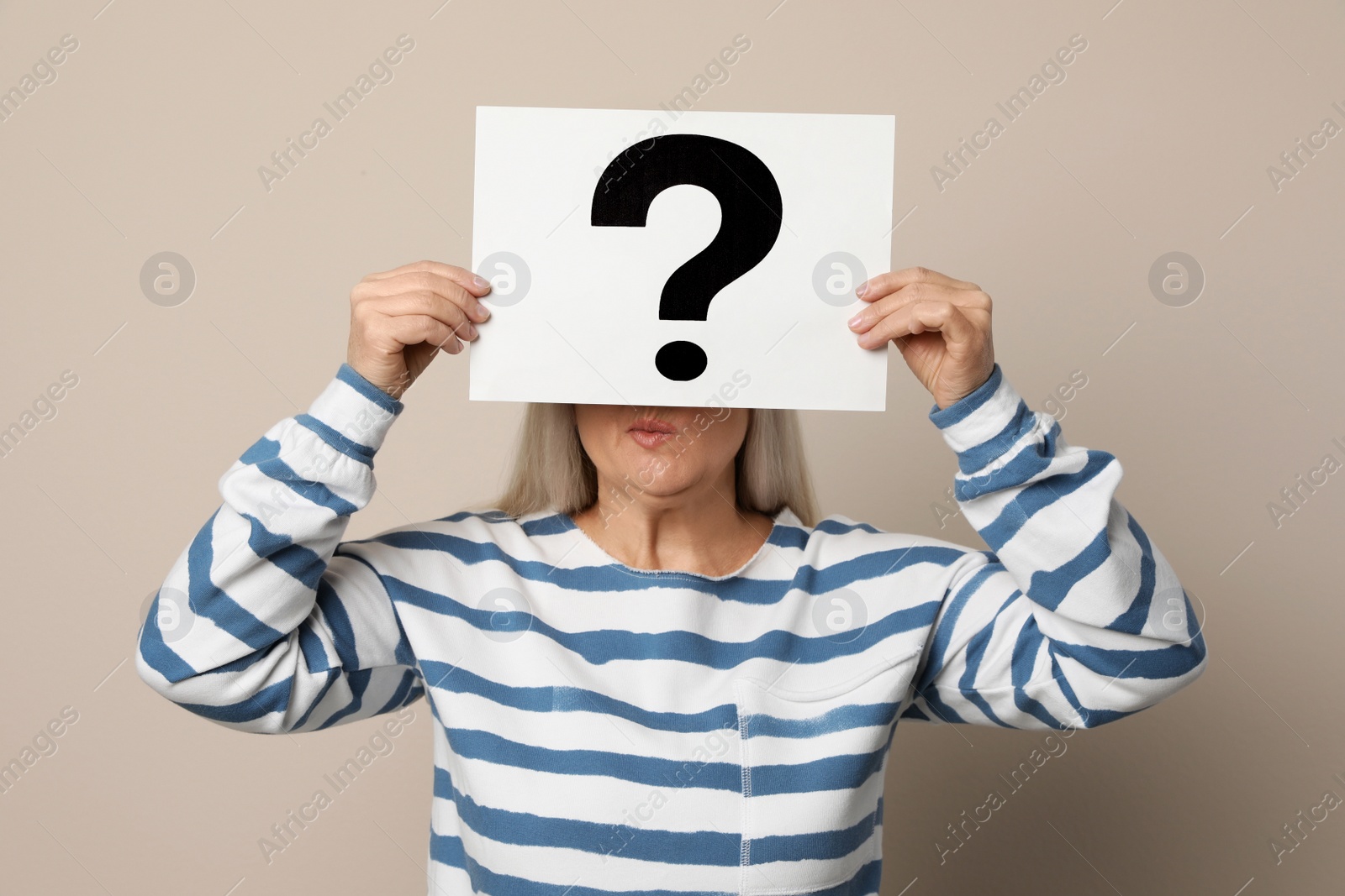 Photo of Mature woman holding paper with question mark on beige background