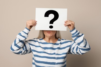 Mature woman holding paper with question mark on beige background