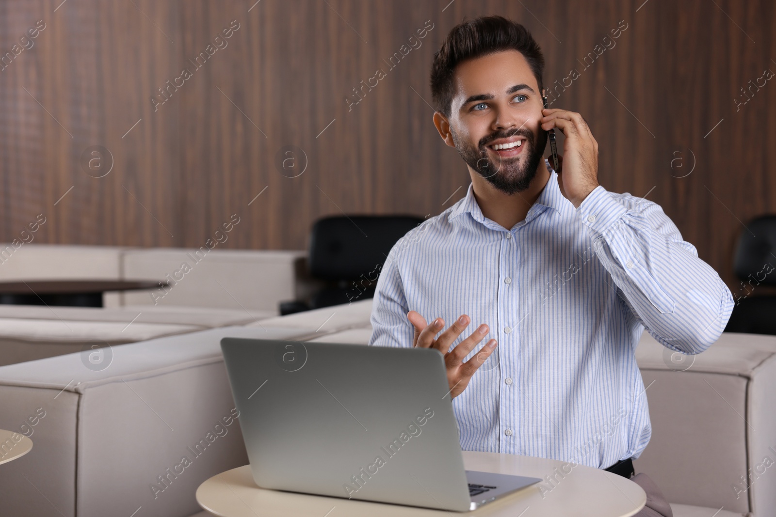 Photo of Happy man using modern laptop while talking on smartphone at table in office. Space for text