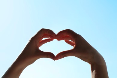 Woman making heart gesture on light blue background, closeup