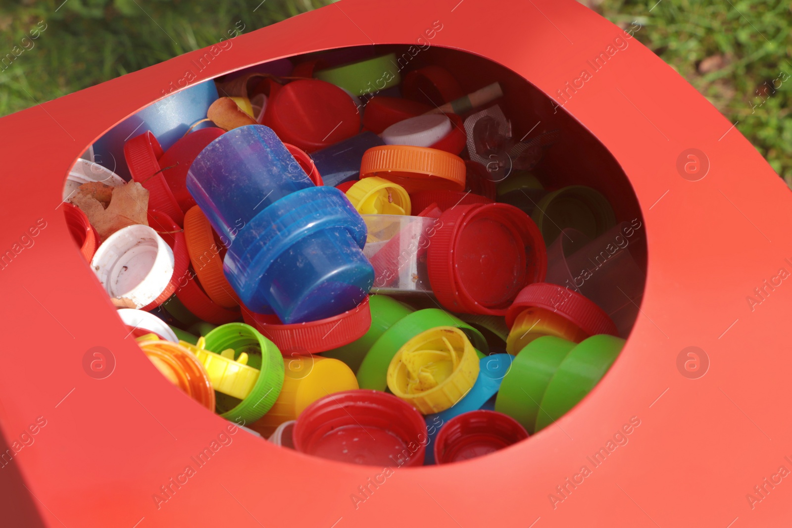 Photo of Different colorful bottle caps in red bin. Plastic recycling