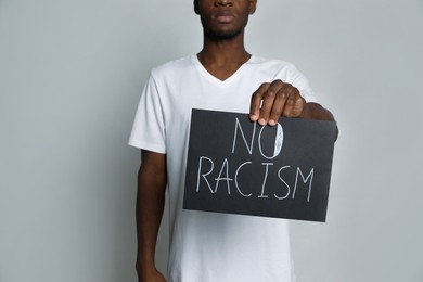 Photo of African American man holding sign with phrase No Racism on grey background, closeup