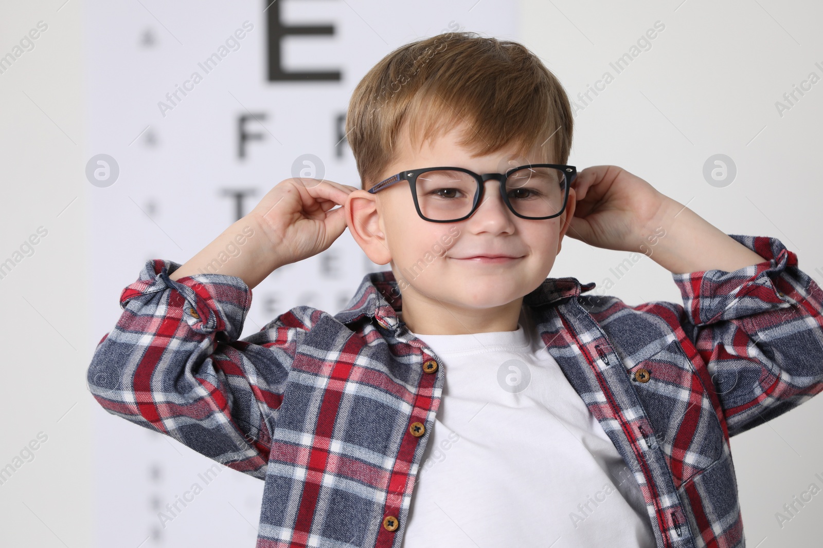 Photo of Little boy with glasses against vision test chart