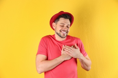 Portrait of handsome man holding hands near his heart on color background