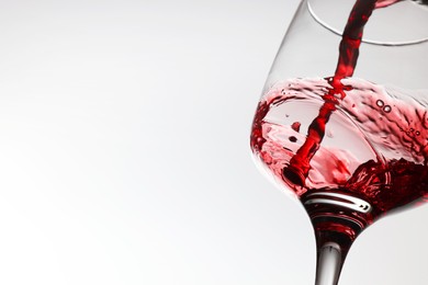 Photo of Pouring tasty red wine in glass on white background, closeup. Space for text