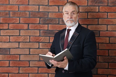 Photo of Serious senior boss in suit with notebook and pen near brick wall. Space for text