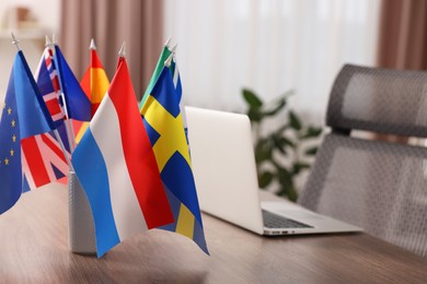 Different flags and laptop on wooden table indoors, selective focus