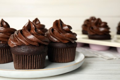 Plate with delicious chocolate cupcakes on white wooden table, closeup