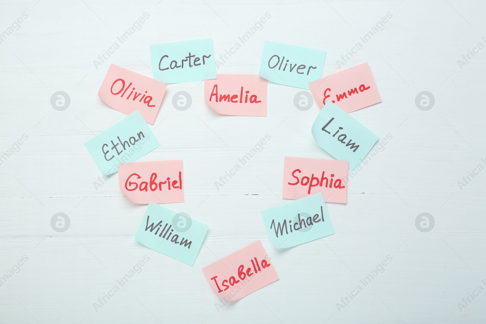 Photo of Choosing baby's name. Heart made of paper stickers with different names on white wooden background, top view