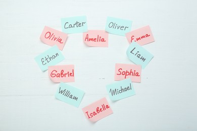 Choosing baby's name. Heart made of paper stickers with different names on white wooden background, top view