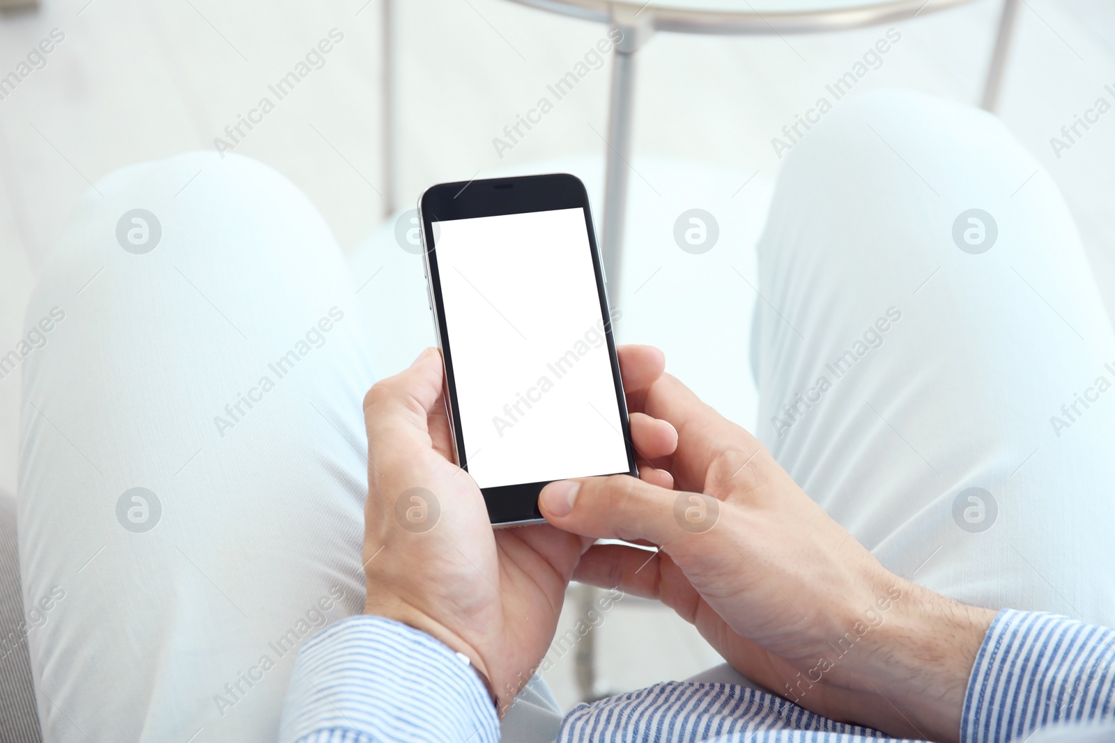 Photo of Young man holding mobile phone with blank screen in hands, indoors