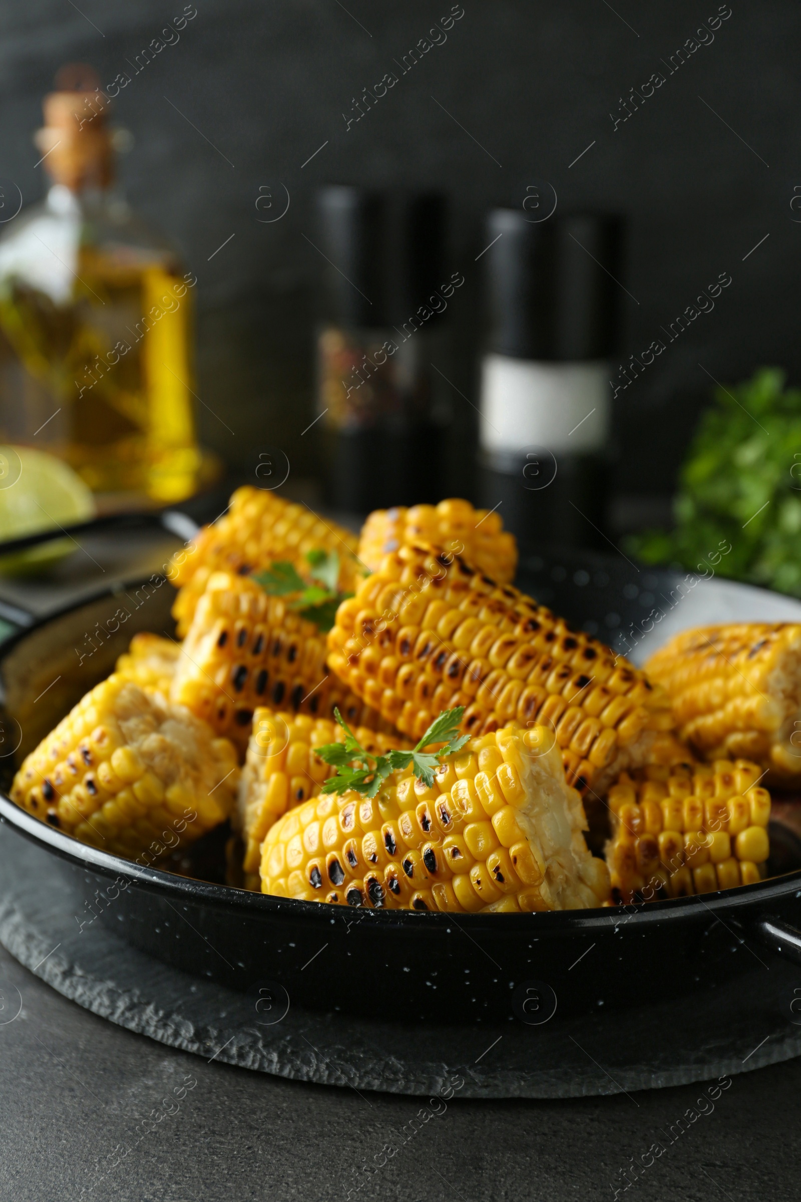 Photo of Pan with tasty grilled corn on dark grey table