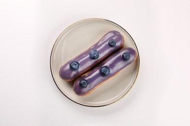 Delicious eclairs decorated with blueberries on white background, top view