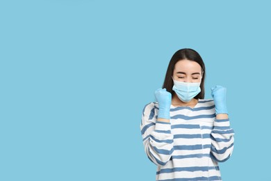 Photo of Emotional woman with protective mask and gloves on light blue background, space for text. Strong immunity concept