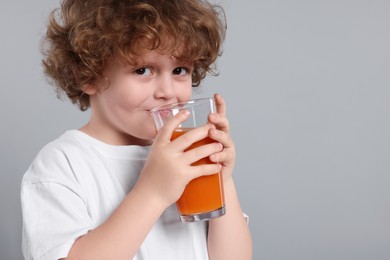 Photo of Cute little boy drinking fresh juice on light gray background, space for text