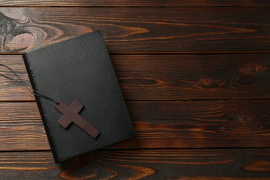 Wooden Christian cross and Bible on table, top view. Space for text