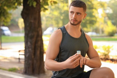 Photo of Attractive serious man checking pulse with blood pressure monitor on finger after training in park. Space for text