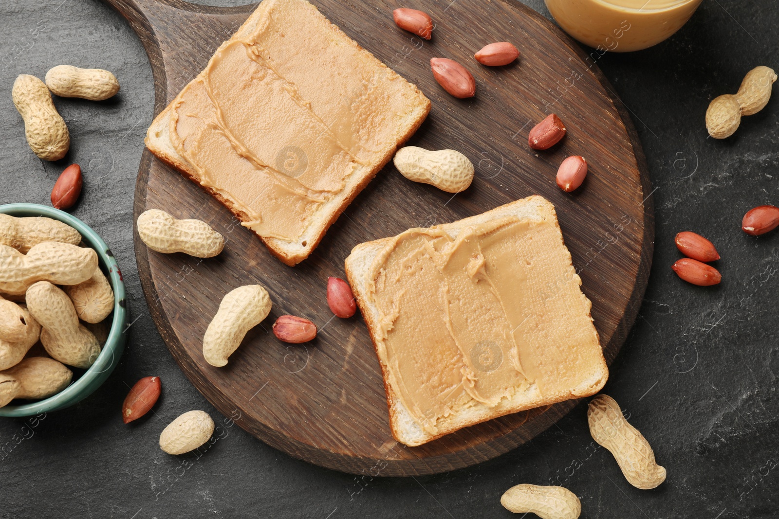 Photo of Tasty peanut butter sandwiches and peanuts on dark gray table, flat lay