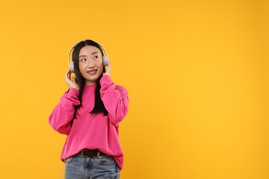 Photo of Portrait of smiling woman in headphones on orange background. Space for text