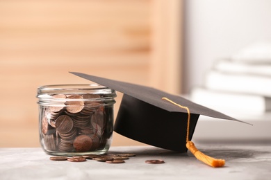 Photo of Jar of coins and graduation hat on table against blurred background. Space for text