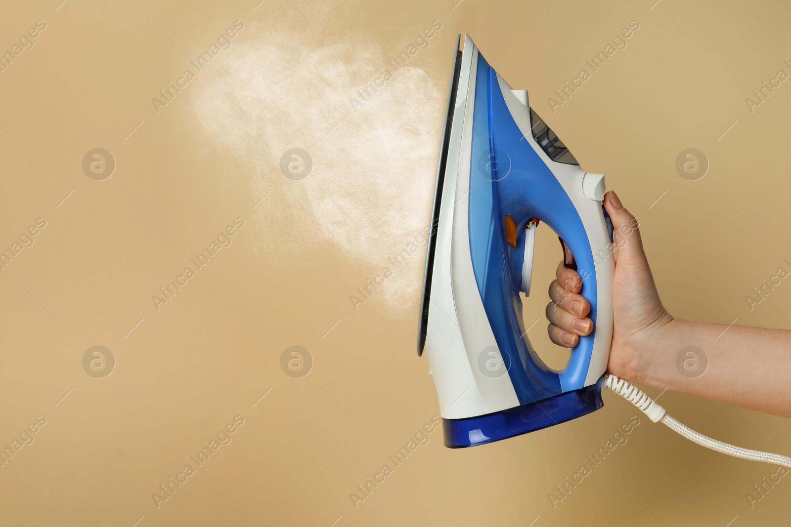 Image of Woman holding modern iron with steam on beige background, closeup. Space for text