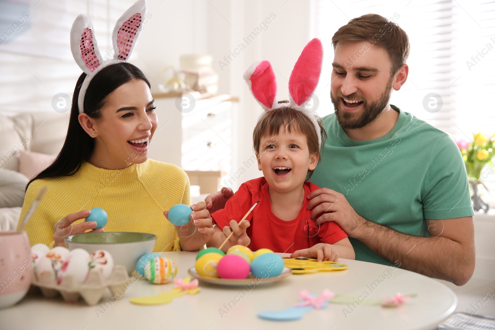 Photo of Happy family painting Easter eggs at table indoors