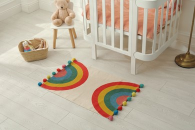 Stylish rug with rainbow on floor in baby room